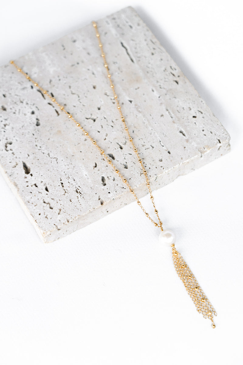Bijou de robe fait d'une chaine à petites billes dorées et une perle naturelle de laquelle pend un pompom de chaines