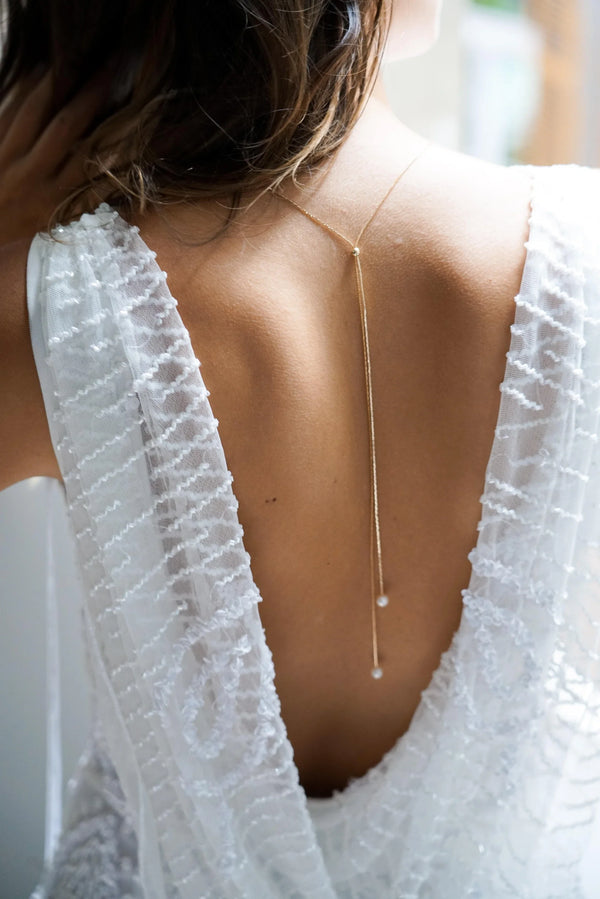 Mariée portant un collier de dos minimaliste doré ajustable avec une double chaine doré et deux perles blanches au bout de chacune