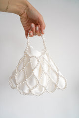 Main portant un sac de mariée blanc à perle et tissu en satin élégant et sophistiqué
