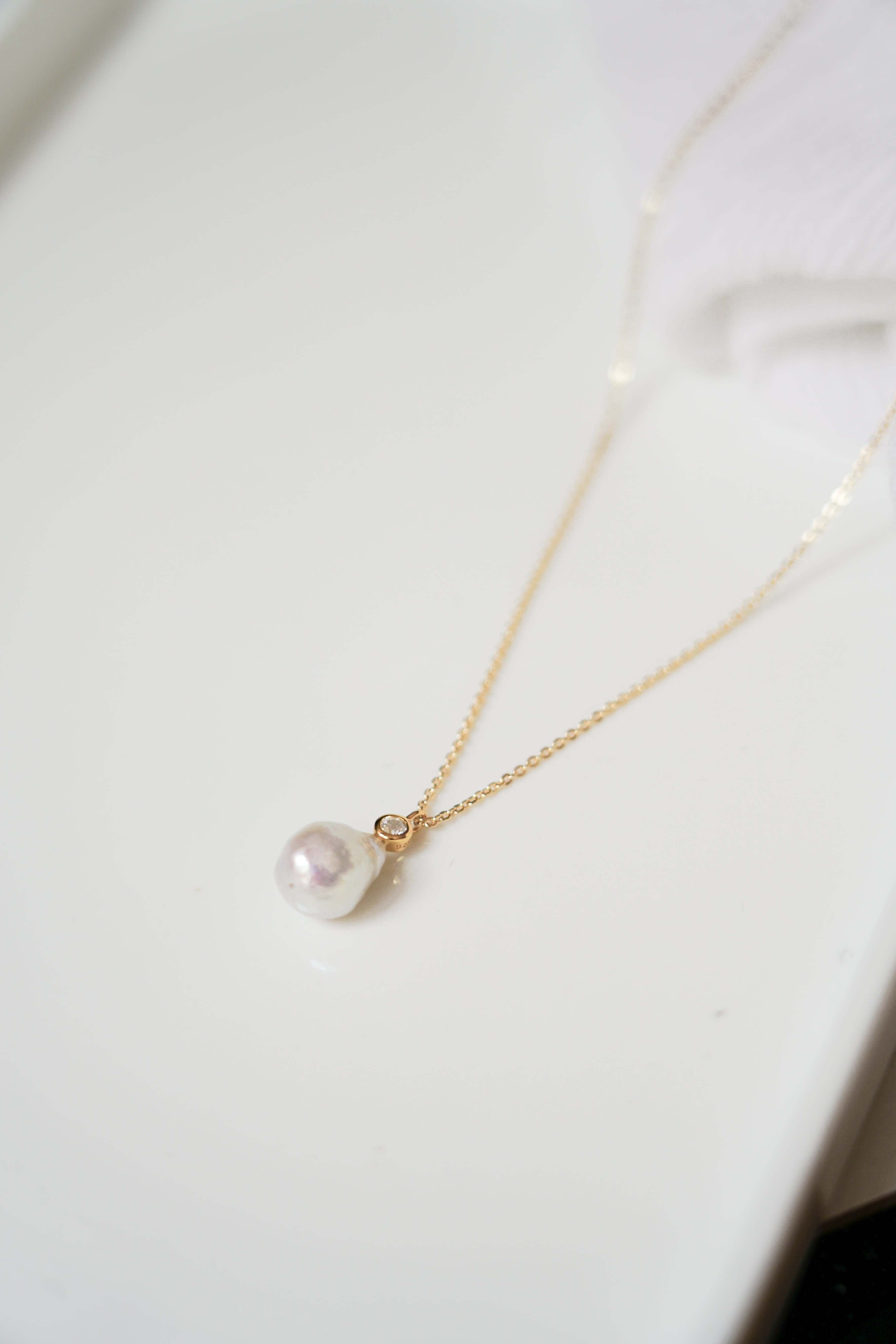 Collier long avec un zircon et une perle baroque bohème sur un fond blanc