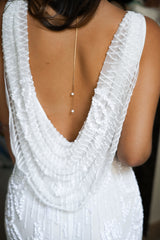 Mariée portant une robe avec un grand décolleté de dos et un collier de dos pendant à double chaînes doré avec des perles au bout 