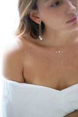 Mariée portant une paire de boucles d'oreilles pendantes à deux chaines dorés et perles rondes au bout et un collier fait d'un fil transparent avec cinq petites perles blanches